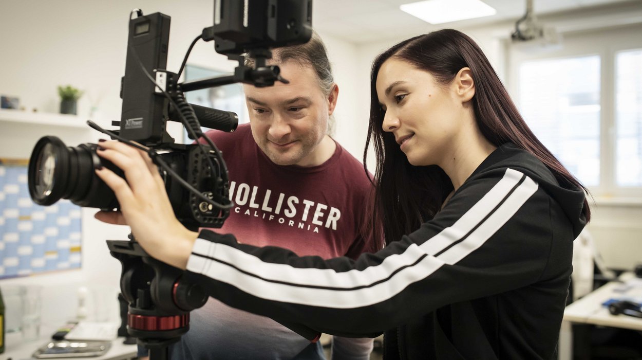 MovieTeam_Jugend-am-Werk-Steiermark Eine junge Frau zeigt einem Mann mit Behinderung die Funktionen einer Kamera.