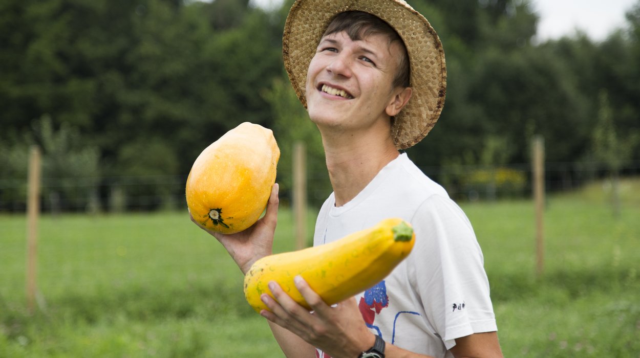 Landwirtschaft-Attendorf_Jugend-am-Werk-Steiermark Junger Mann mit Behinderung mit Kürbissen in Händen auf einem Feld der ökologischen Landwirtschaft.