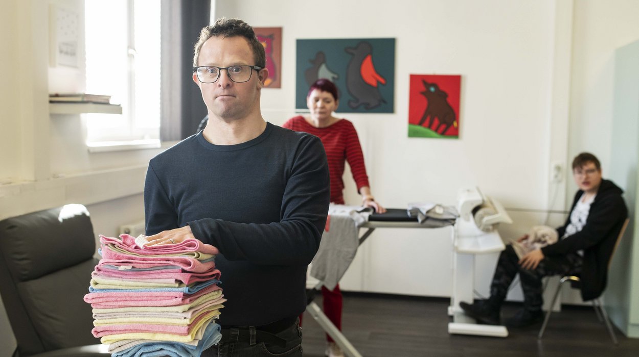 Waesche-und-Buegelservice_Jugend-am-Werk-Steiermark Mensch mit Behinderung mit einem Wäschestapel in den Händen.
