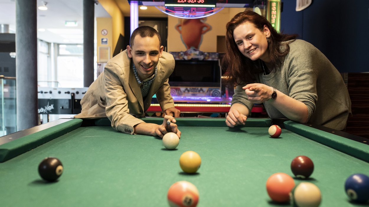 Eine Frau und ein Mann mit Behinderung spielen gemeinsam Billard
