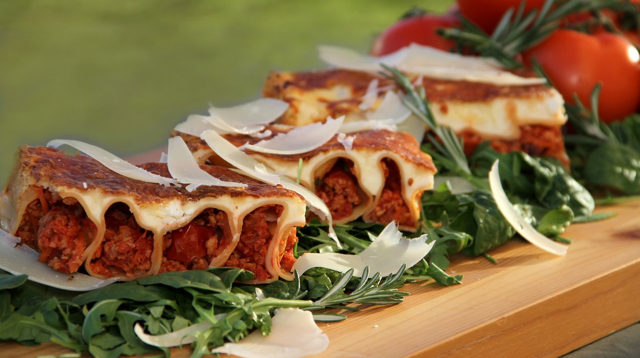 Essen-fuer-Schulen-und-Kindergaerten_Jugend-am-Werk-Steiermark Lasagne mit Salatdekoration auf einem Holzbrett.