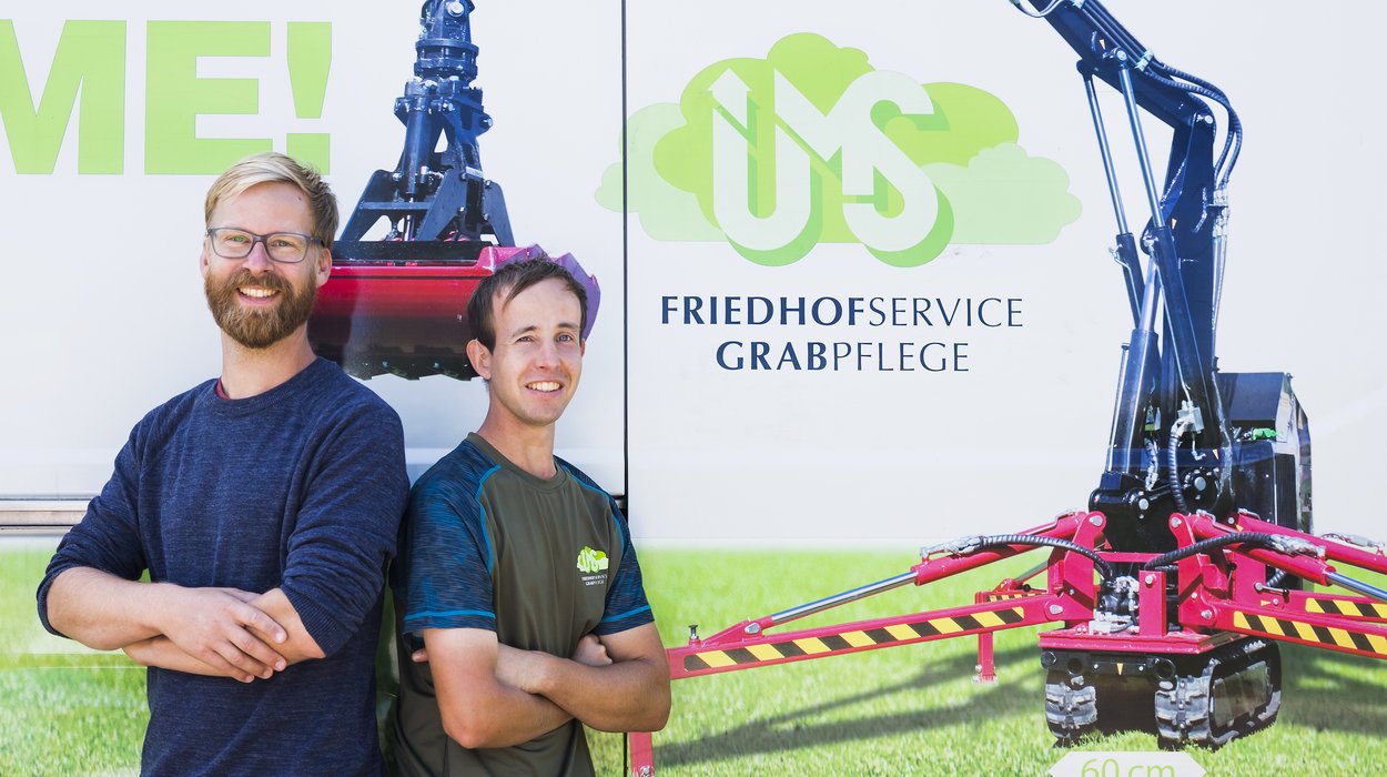 inArbeit Arbeitsplaetze für Menschen mit Behinderung Verantwortlicher von UMS und Mitarbeiter mit Behinderung stehen vor einem Plakat