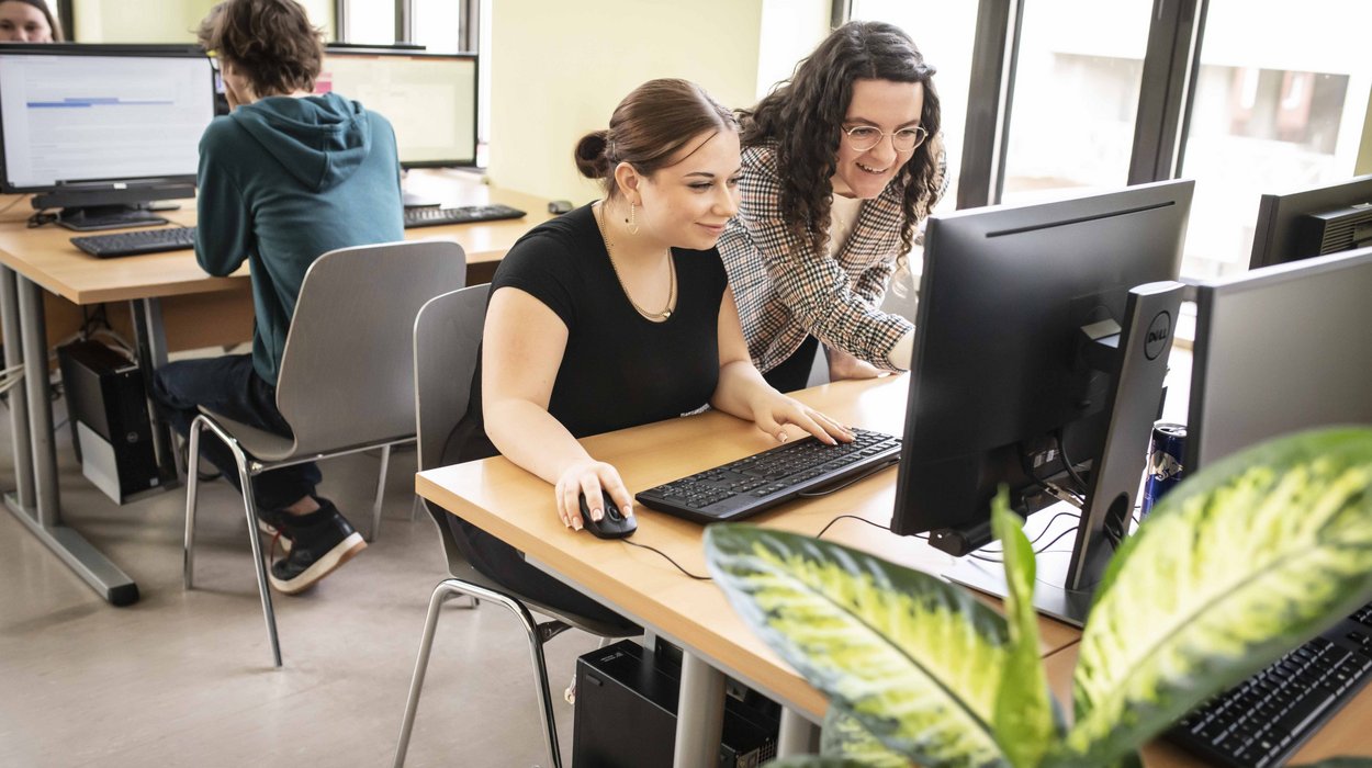 Praktikum_Jugend-am-Werk-Steiermark Eine Mitarbeiterin unterstützt eine Jugendlichen vor einem Computer.