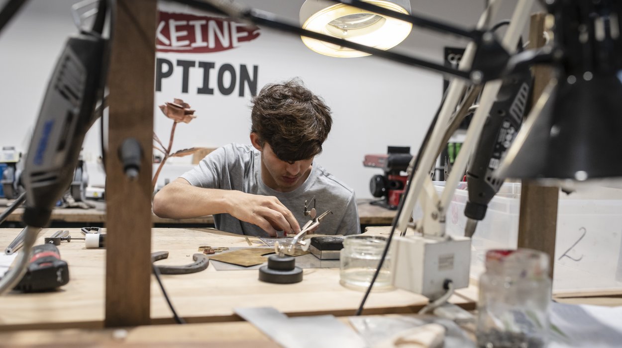 Produktionsschule bei Jugend am Werk Steiermark Jugendlicher sitzt an der Werkbank und gestaltet etwas aus Metall