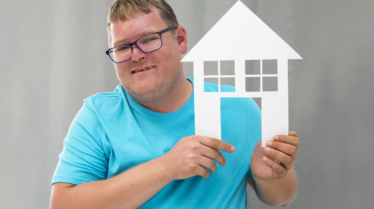 ein Mann mit Behinderung hält freudig ein Papierhaus in der Hand