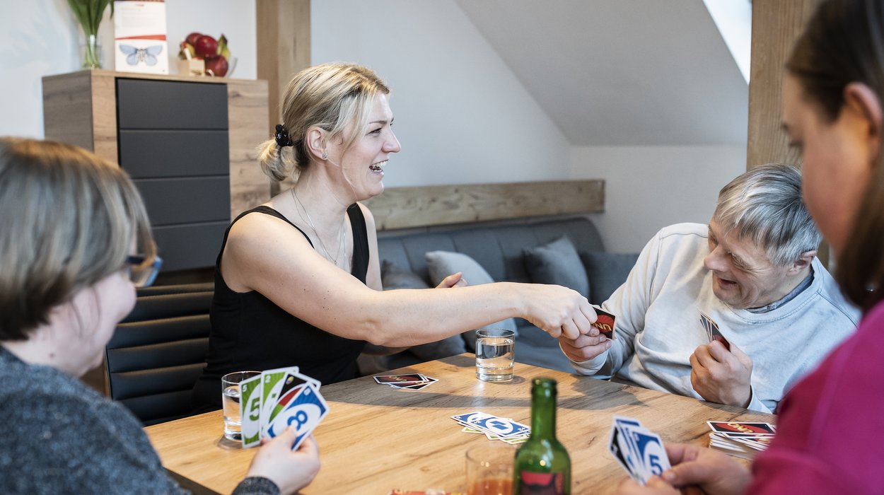 Eine Begleiterin spielt mit 3 Menschen mit Behinderung Uno