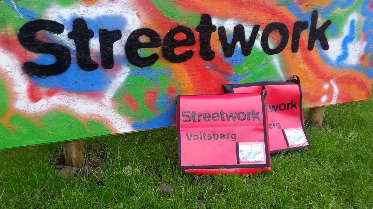 Zwei rote Taschen auf dem Boden vor einer bunt bemalten Wand, auf der das Wort "Streetwork" steht