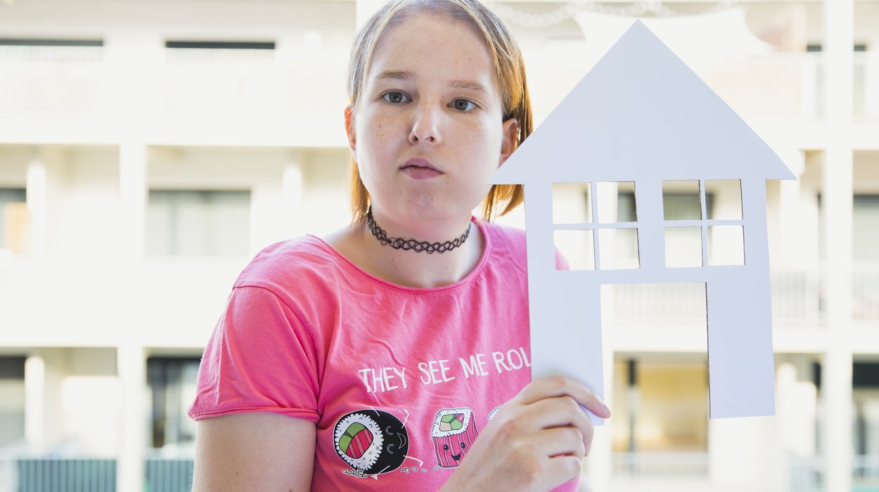 ein Mädchen mit Behinderung hält ein Papierhaus in der Hand