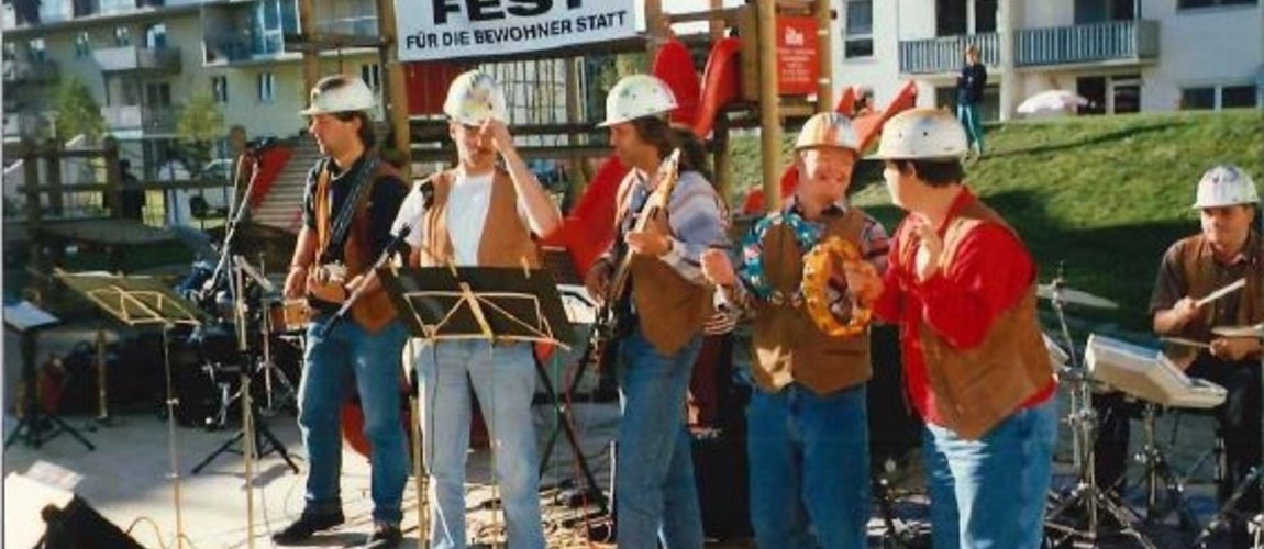 Eine Band bestehend aus Menschen mit Behinderung spielt auf einem Fest, alle tragen Bauhelme