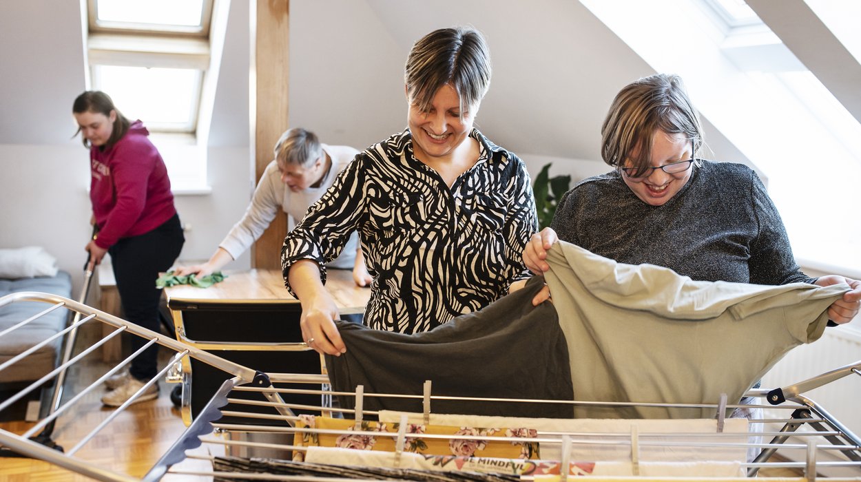 Eine Frau mit Behinderung und eine Betreuerin hängen gemeinsam Wäsche auf.