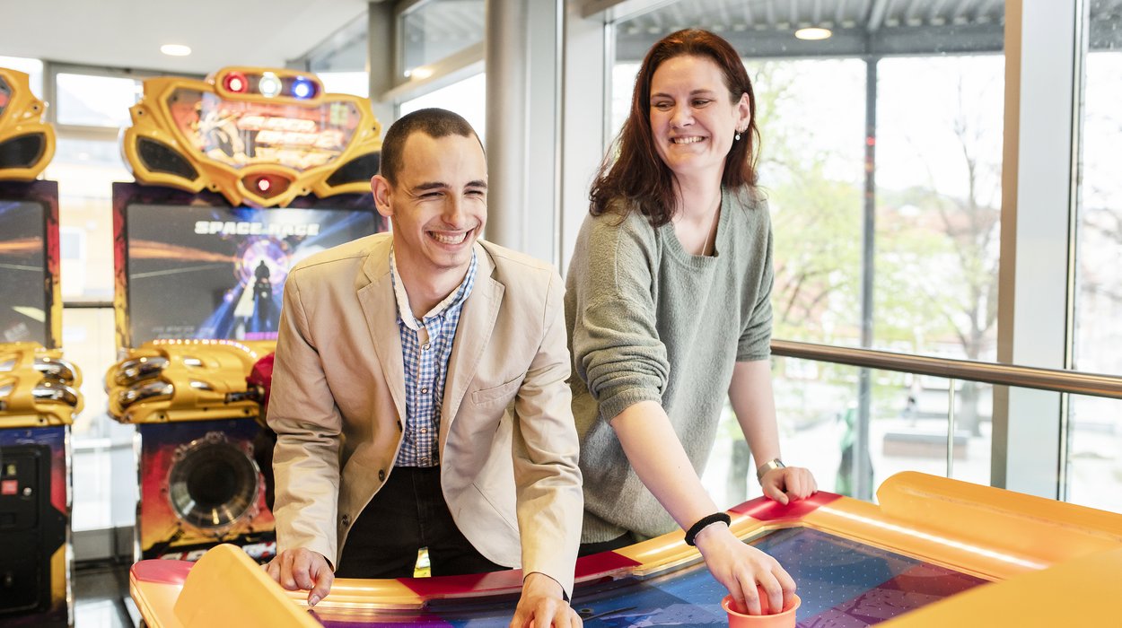 Eine Frau und ein Mann mit Behinderung verbringen gemeinsam Freizeit in einer Spielehalle