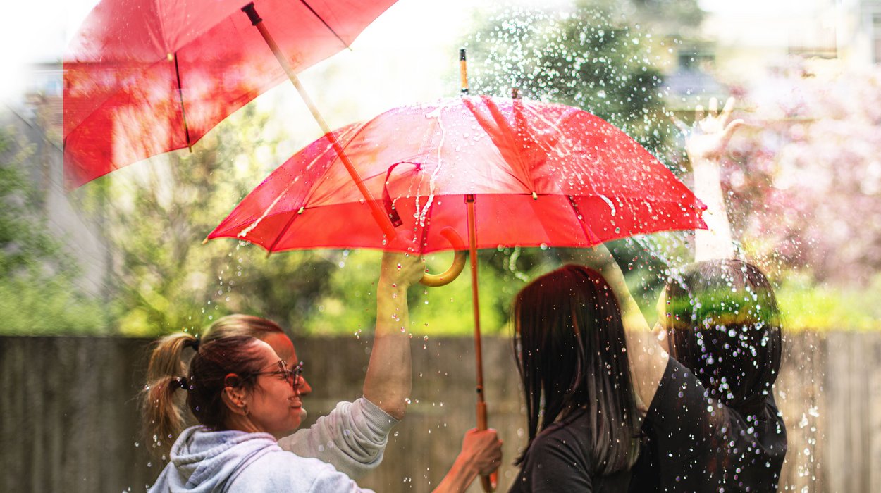 Eine Frau hält einen roten Regenschirm über zwei Jugendliche