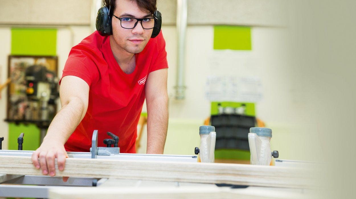 Überbetriebliche Lehrausbildung bei Jugend am Werk Steiermark Jugendlicher mit Brille trägt Gehörschutz und arbeitet in einer Lehrwerkstätte mit Holz