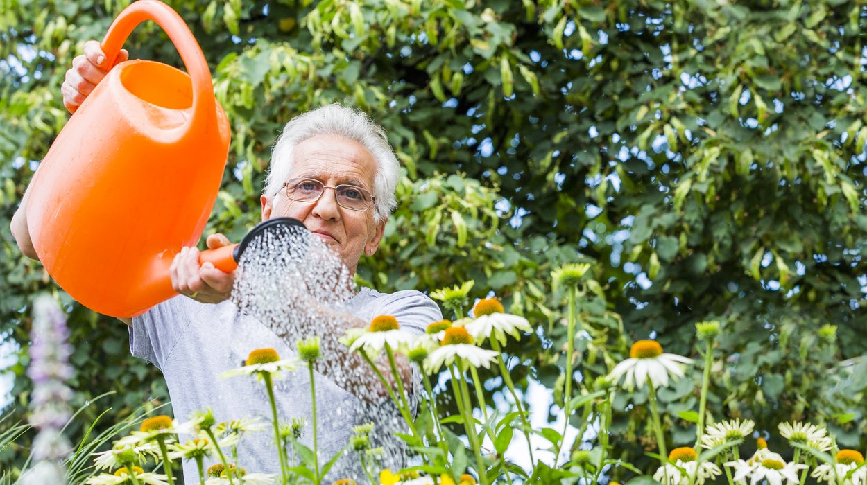Gemeinnuetzige-Beschaeftigung_Jugend-am-Werk-Steiermark Mann mit oranger Gießkanne wässert Blumen in einem Garten