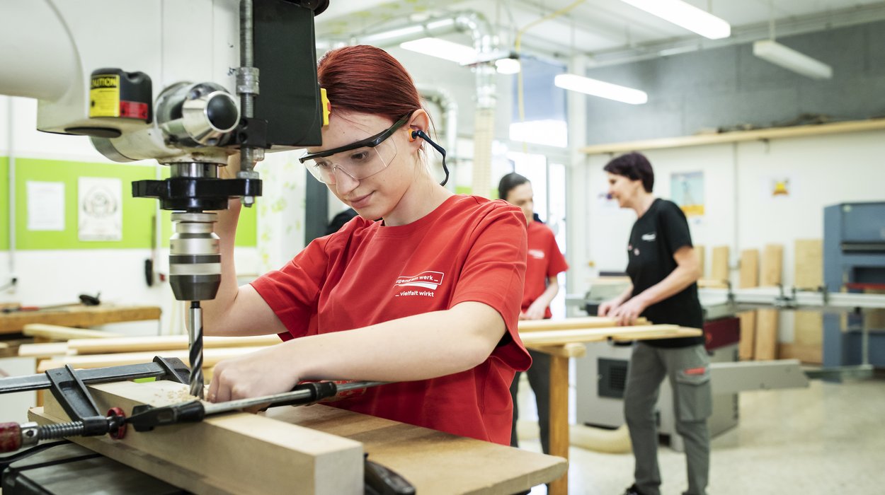 Ein Mädchen bohrt an einer Werkbank mit einer Maschine Löcher in Holz