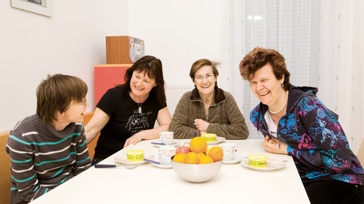 vier Personen sitzen lachend am Esstisch