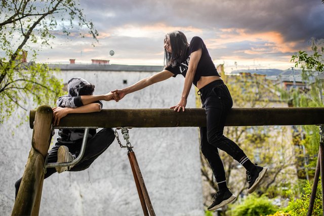 Zwei Jugendliche auf einem Schaukelgerüst, eine hilft dem anderen nach oben Zwei Jugendliche auf einem Schaukelgerüst, eine hilft dem anderen nach oben