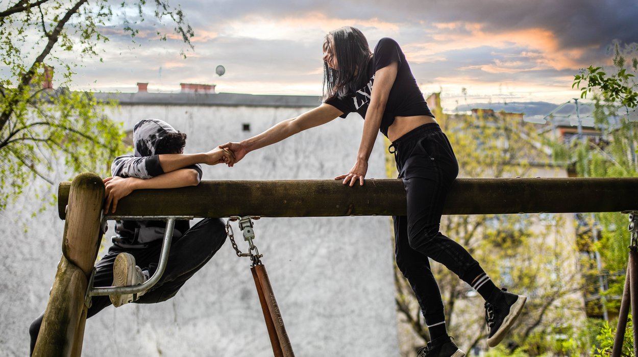 Zwei Jugendliche auf einem Schaukelgerüst, eine hilft dem anderen nach oben