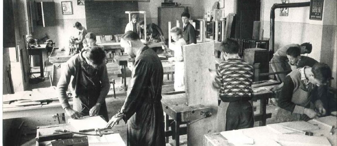 Ein schwarzweißes Foto, das Jugendliche und Fachtrainer in einer Holzwerkstatt zeigt