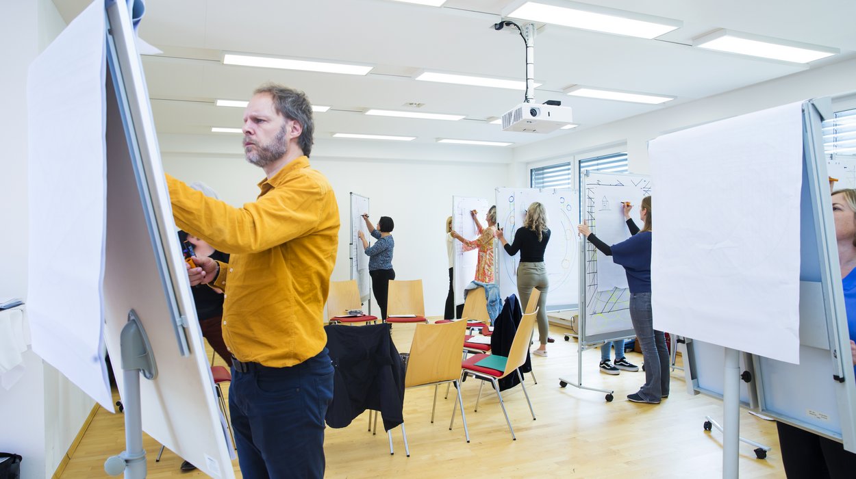 inbildung_Jugend-am-Werk-Steiermark Mehrere Personen arbeiten in einem hell erleuchteten Seminarraum an Flipcharts
