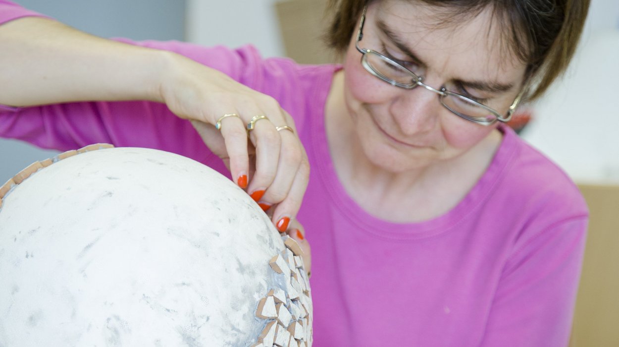 Teilhabe an Beschaeftigung bei Jugend am Werk Steiermark Frau mit Behinderung dekoriert eine Keramikkugel