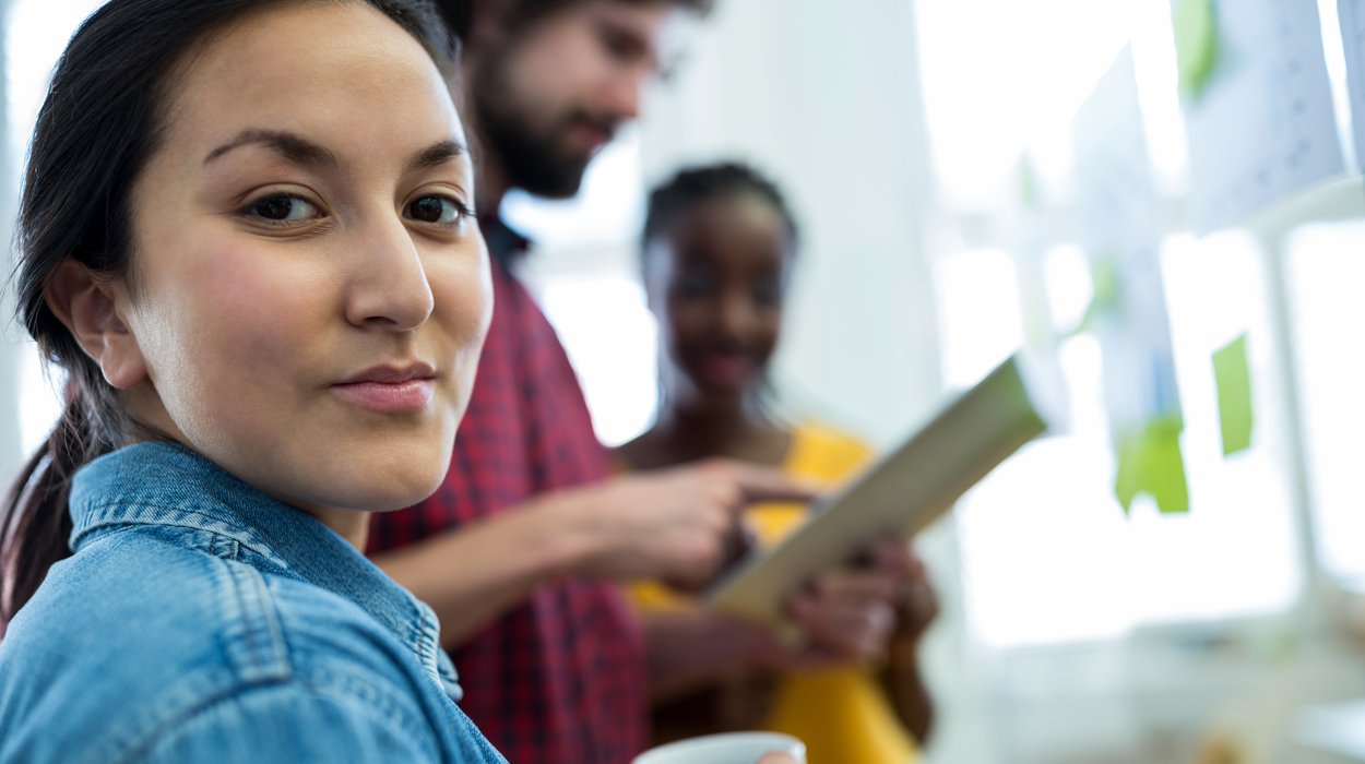 Bildungsmaßnahmen-Hartberg_Jugend-am-Werk_shutterstock Frau mit Kaffeetasse in einem Büro, im Hintergrund Kollegen